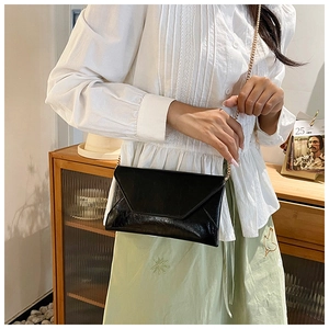 Detail of a black glossy envelope crossbody bag with a gold metal chain strap for women