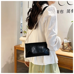 Detail of black envelope crossbody bag with vintage texture and gold chain strap
