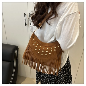 Close-up of brown suede crossbody bag featuring gold rivets and bohemian fringe details