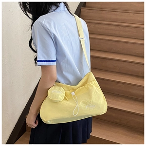 Detail of yellow nylon crossbody bag with drawstring pocket and mini round coin purse charm