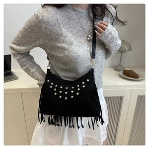 Detail of black suede saddle bag featuring gold rivets and long tassels on a model