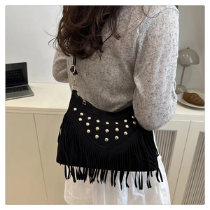 Close-up of black fringe shoulder bag with gold studs worn by a model in an indoor setting