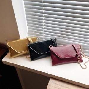 Three minimalist envelope crossbody bags with chain straps in gold black and burgundy colors