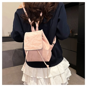 Back view of a woman wearing a light pink wrinkled leather backpack with drawstring closure