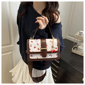 Détail du sac bandoulière blanc avec imprimés cerises et breloque en métal doré