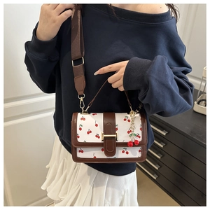 Detail of crossbody square bag with cherry print, brown leather trim, and cherry charm