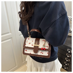 Detail of a white crossbody bag with red cherry print and leather trim on a female model