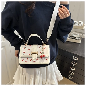 Chic white crossbody bag with red cherry prints and wide shoulder strap on a model