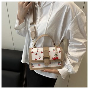 Detail of white cherry print square bag with beige trim and dual cherry metal pendant