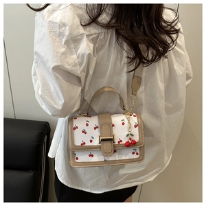 Close-up of white crossbody bag with cherry print, gold buckle, and cherry charm detail