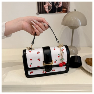 Dettaglio di una borsa a tracolla bianca con stampe di ciliegie e ciondolo decorativo
