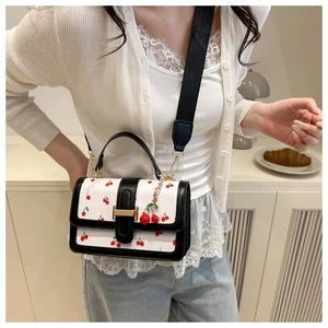 Close-up of a white cherry print crossbody bag with black trim and a wide fabric strap