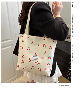 Detail of cream corduroy tote bag with cherry embroidery and fashion label on black blazer