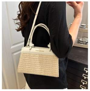 Detail of beige woven and white leather crossbody bag with dual handles and gold lettering