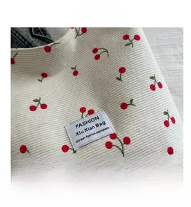 Macro detail of white corduroy tote bag featuring cherry embroidery and fashion woven label