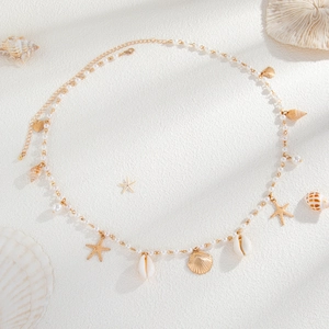 Detail of beach body chain with gold starfish shells and pearls on sand texture