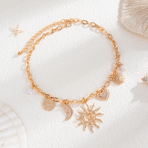 Gold celestial charm bracelet with sun, moon, and pearl details on a beach setting