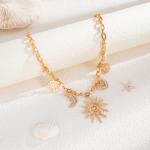 Detail of gold necklace with sun and starfish charms against beach-themed props
