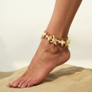 Golden beach anklet with starfish shells and pearls on a woman foot in the sand