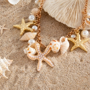 Golden beach anklet with starfish, conch, and pearls on a white sandy background