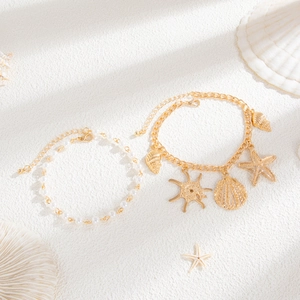 Detailed shot of starfish and seashell charms on gold-tone layered anklet set with pearls