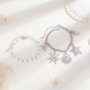 Detail of beach-style jewelry set with pearl beads, starfish and shell charms on sand