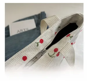 Detail view of smooth metal zipper on white corduroy tote bag with cherry patterns