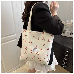 Detail of white corduroy tote bag featuring cherry patterns and woven fashion label