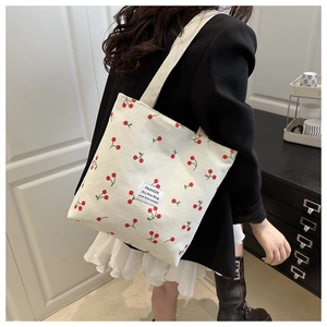 Detail of white corduroy tote bag featuring cherry prints and woven fashion label