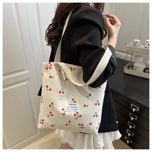 Detail view of corduroy tote bag with cherry prints on a model in a casual setting
