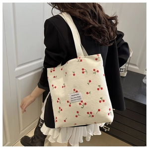 Detail of cream corduroy tote bag with red cherry patterns worn with a black blazer
