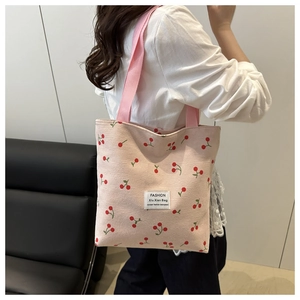 Detail of light pink corduroy tote bag with cherry print and white fabric brand label