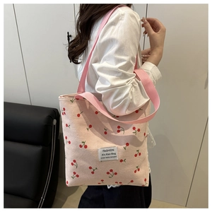 Close-up of pink cherry print corduroy tote bag with woven straps and logo patch