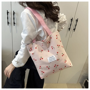 Pink corduroy tote bag with cherry prints and a white brand label shown on a model