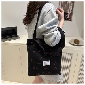Detail of black corduroy tote bag with red cherry patterns and long shoulder strap