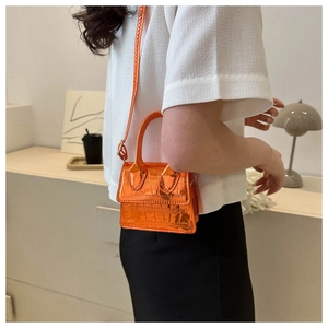 Detail of bright orange crocodile pattern mini bag with metallic finish and top handle