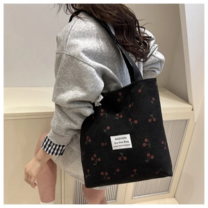 Detail of black corduroy tote bag with red cherry embroidery and fashion label strap