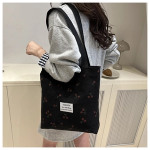Model wearing a black corduroy tote bag with red cherry embroidery and fashion label