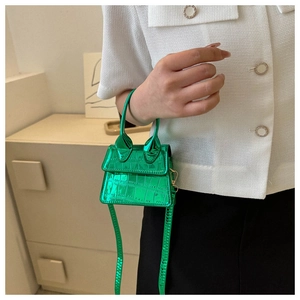 Hand holding a mini bright green crocodile embossed micro bag with top handle and strap