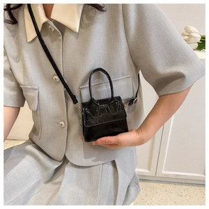 Detailed view of mini black crocodile pattern leather bag with glossy finish on a grey suit