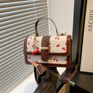 Elegante borsa a tracolla crema con stampa ciliegia e finiture in pelle marrone in mano