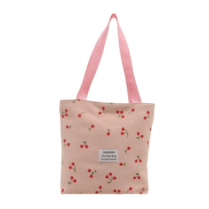 Pink corduroy tote bag with red cherry prints and woven label on a white background