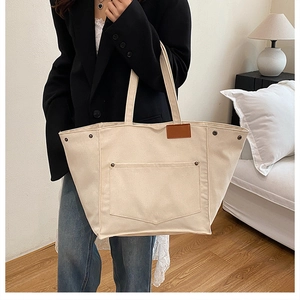 Detail shot of a large beige canvas tote bag with brown leather tag and metal rivets