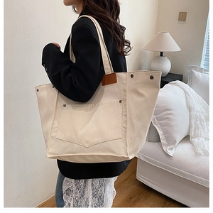 Detail of canvas tote bag showing large front pocket with brown leather trim and rivet