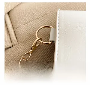 Close-up of golden metal lobster clasp and chain details on a white leather handbag