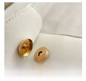 Detail of white lychee grain leather bag showing the gold magnetic snap button closure