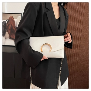 Close-up of white envelope bag with crescent gold buckle and metallic chain strap