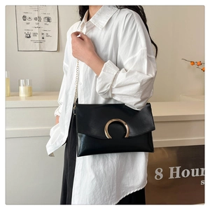 Detail of black envelope bag with golden horseshoe clasp and sleek metal chain strap