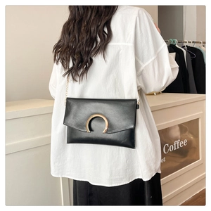 Detailed view of black leather envelope bag with gold buckle and chain strap on a model