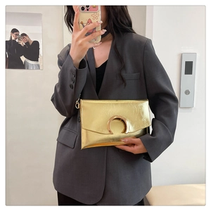 Mirror selfie showing the golden metallic envelope clutch with horseshoe buckle on a suit